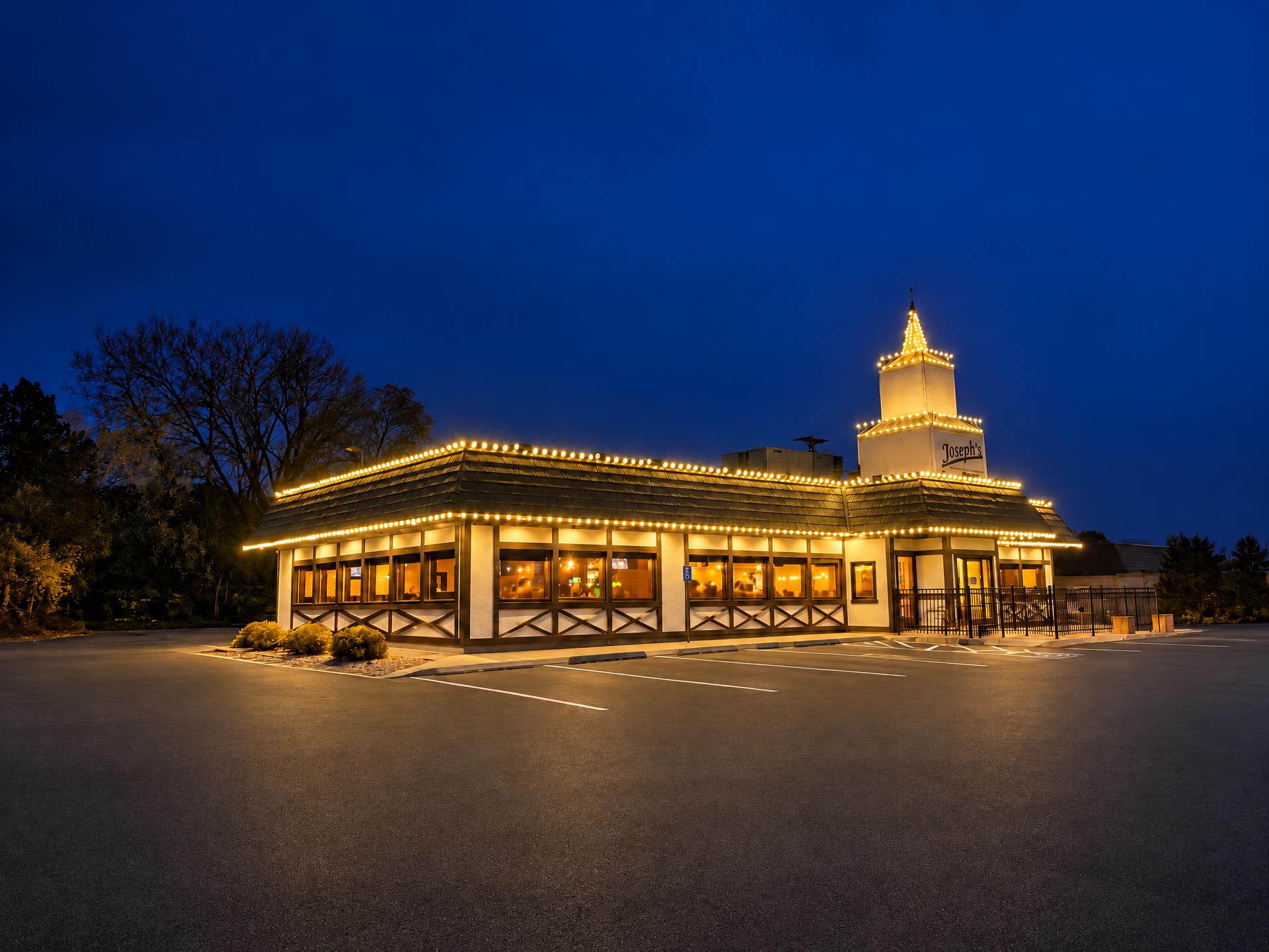 Restaurant building at dusk with warm white lights outlining the mansard roof and the rooftop tower, standing behind an empty parking lot